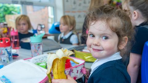Pupils eating their packed lunches a young girl eating a banana smiles for the camera