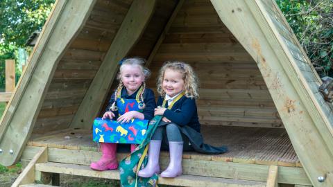 Two girl from early years chat in and outdoor shelter